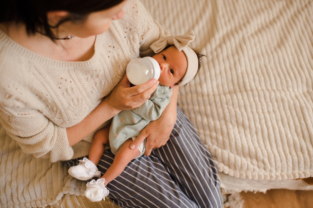 Mother bottle-feeding baby while sitting on a couch