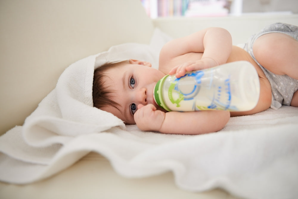 Baby lying on a blanket drinking breast milk from a bottle
