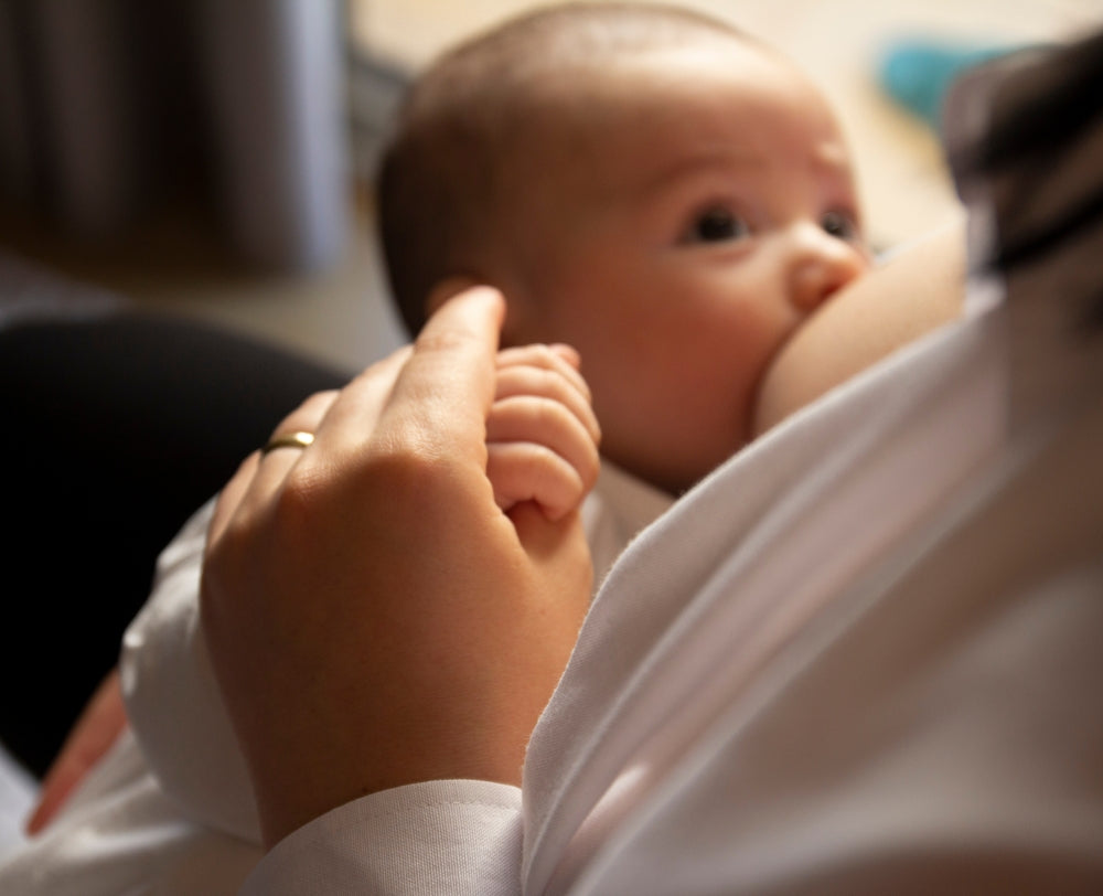 Baby breastfeeding while holding a parent’s hand